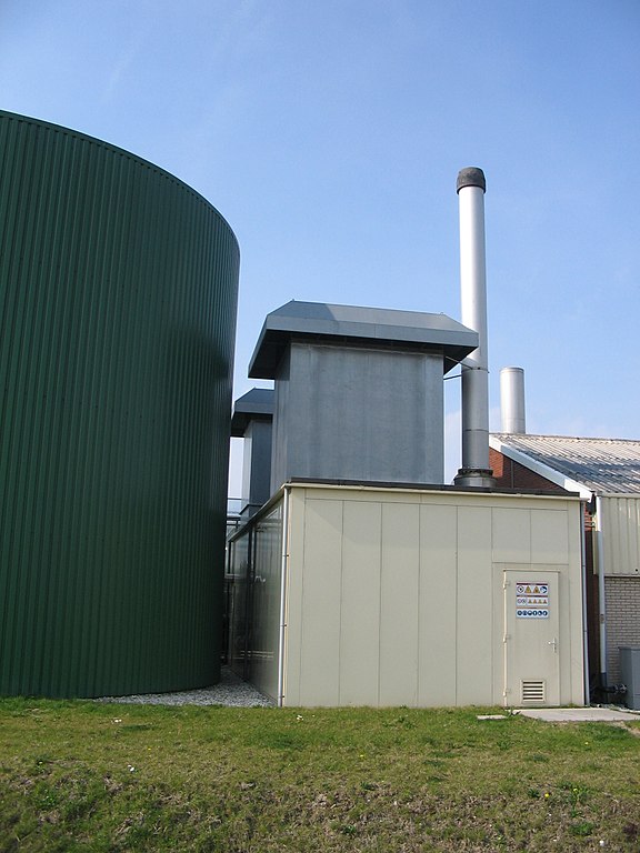 “Een WKK (midden) en warmteopslagtank (links) van een glastuinbouwbedrijf in De Lier.” Door Druifkes (2009), via Wikipedia.